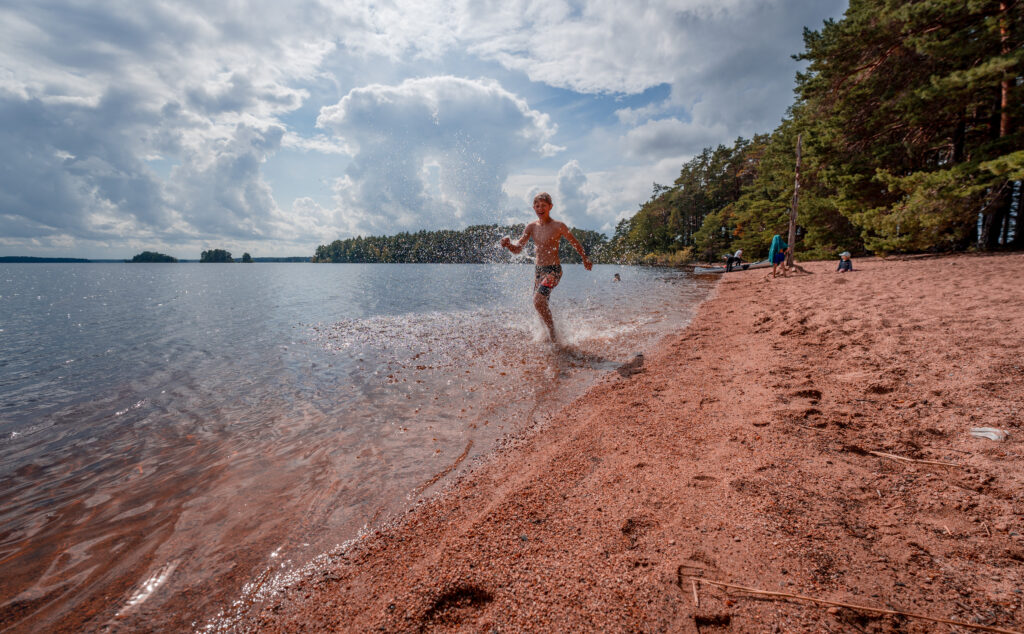 Farnebofjarden-National-Park-Family-hike-camping-kayak-sandon-kid-running-in-water-on-beach-scaled